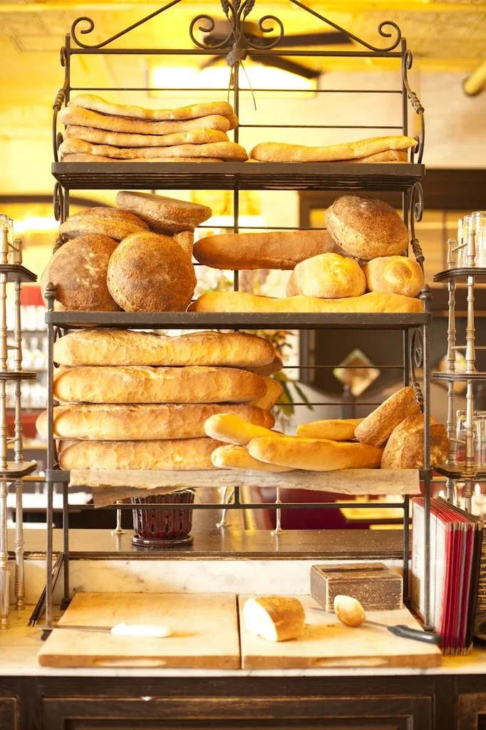 Tiered wrought-iron rack displaying various fresh breads, with knife and butter.