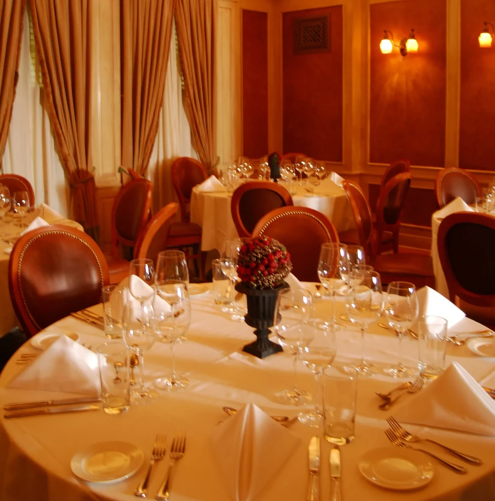 Elegant restaurant dining room, set tables, warm lighting, reddish-brown decor.