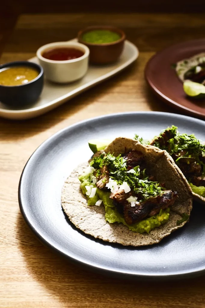 Two meat tacos with guacamole, onion, cilantro on a wooden table.