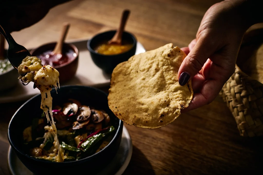 Grilled tortilla and cheesy vegetable dish with a fork pulling cheese.