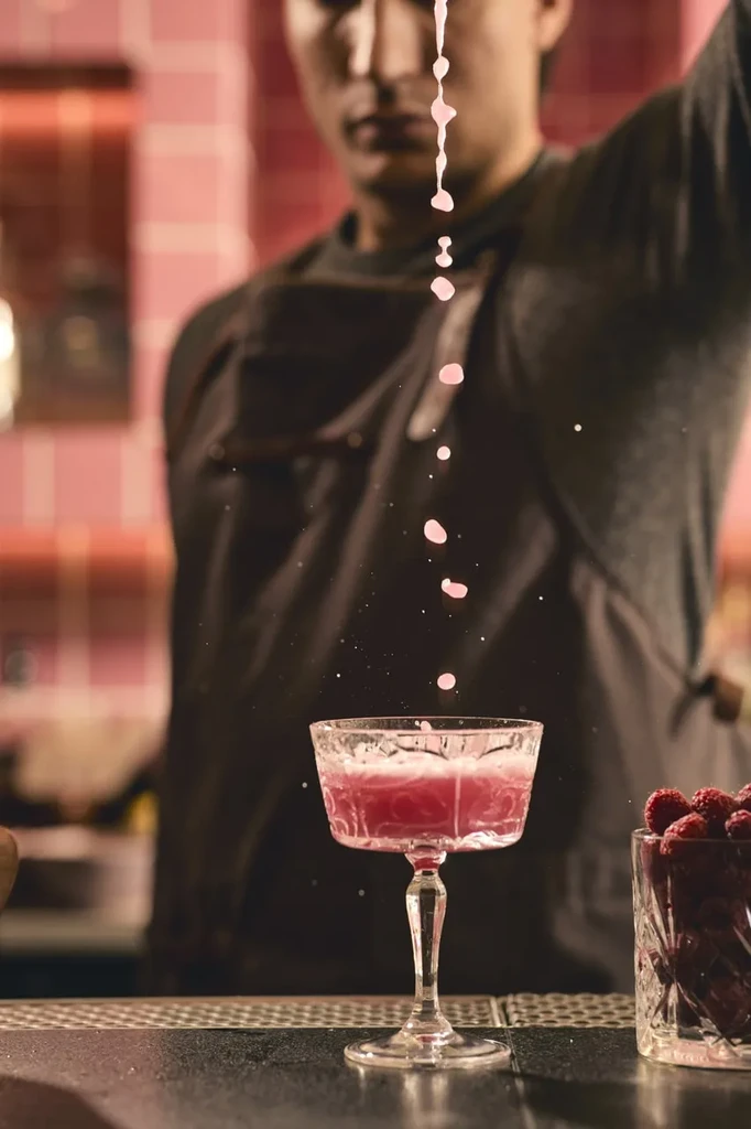 Pink cocktail poured into a stemmed glass, with raspberries.