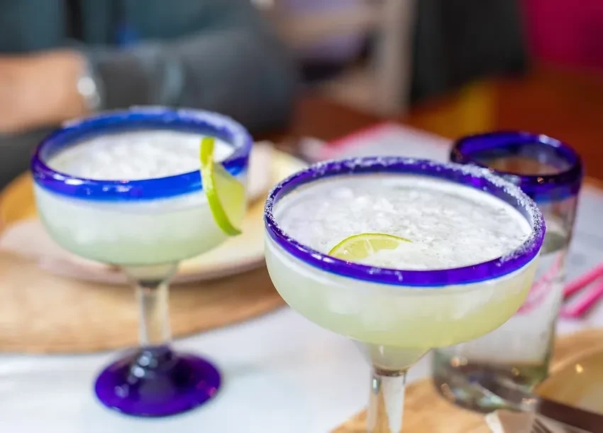 Two frosty margaritas in blue-rimmed glasses with lime.