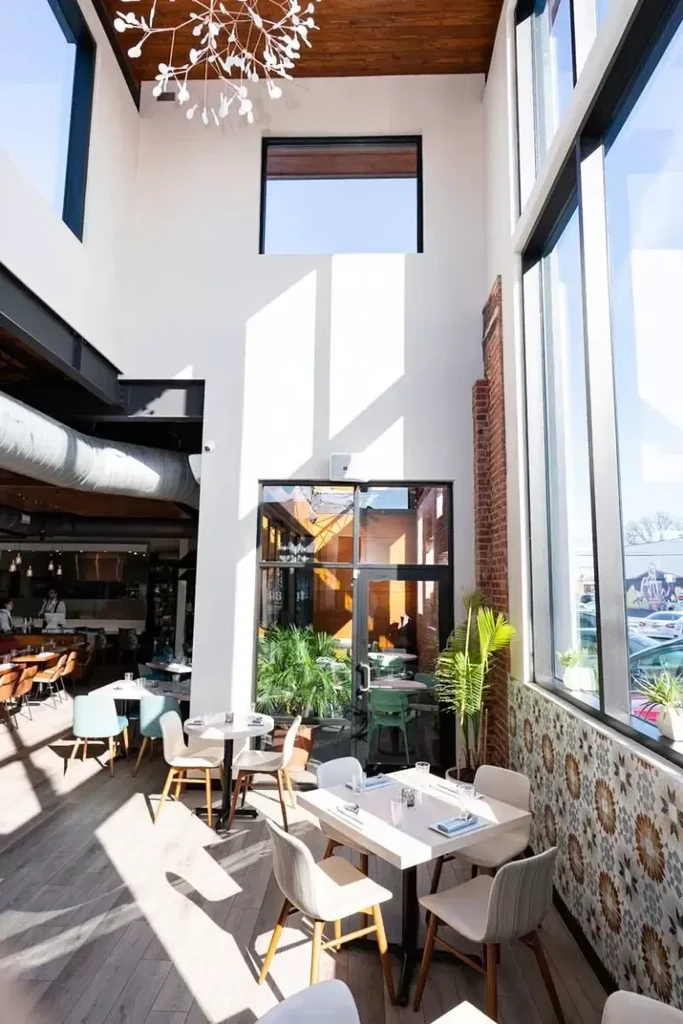 Modern restaurant dining area with natural light, light furniture, and plants.