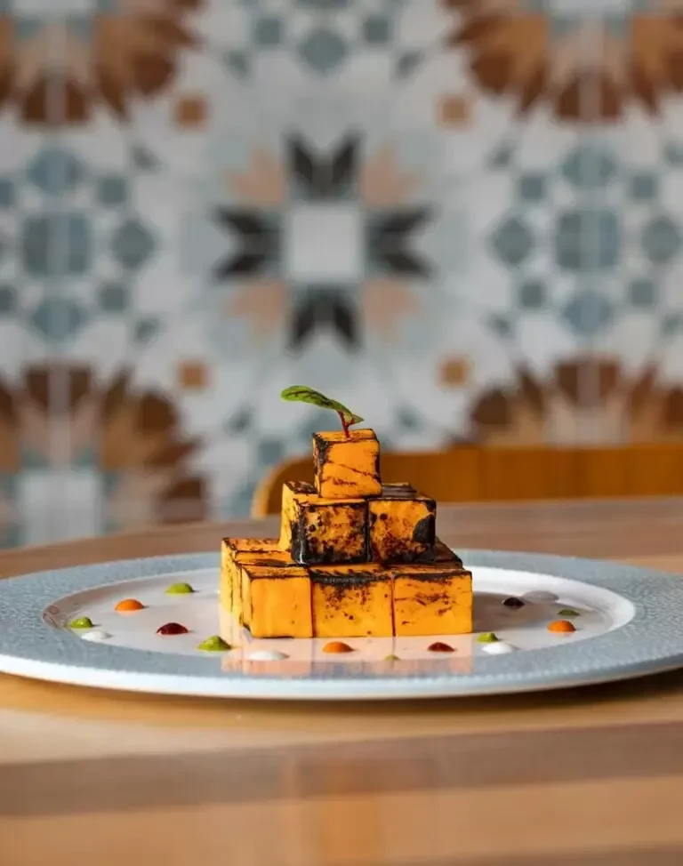 Seared orange-yellow food blocks stacked pyramid-style with colorful sauces.