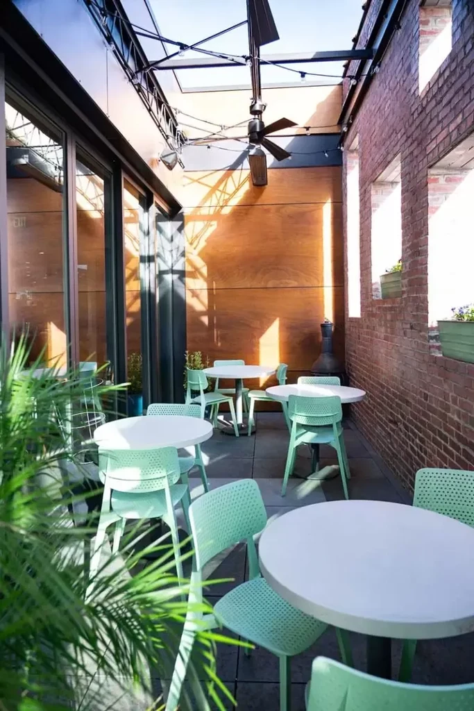 Restaurant patio with mint green chairs, round tables, brick wall, and plants.