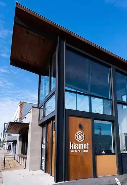Kismet Modern Indian restaurant exterior: modern, glass, wood, under blue sky.