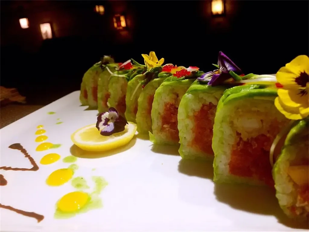 Eight avocado sushi rolls garnished with roe, edible flowers, sauces, and lemon.