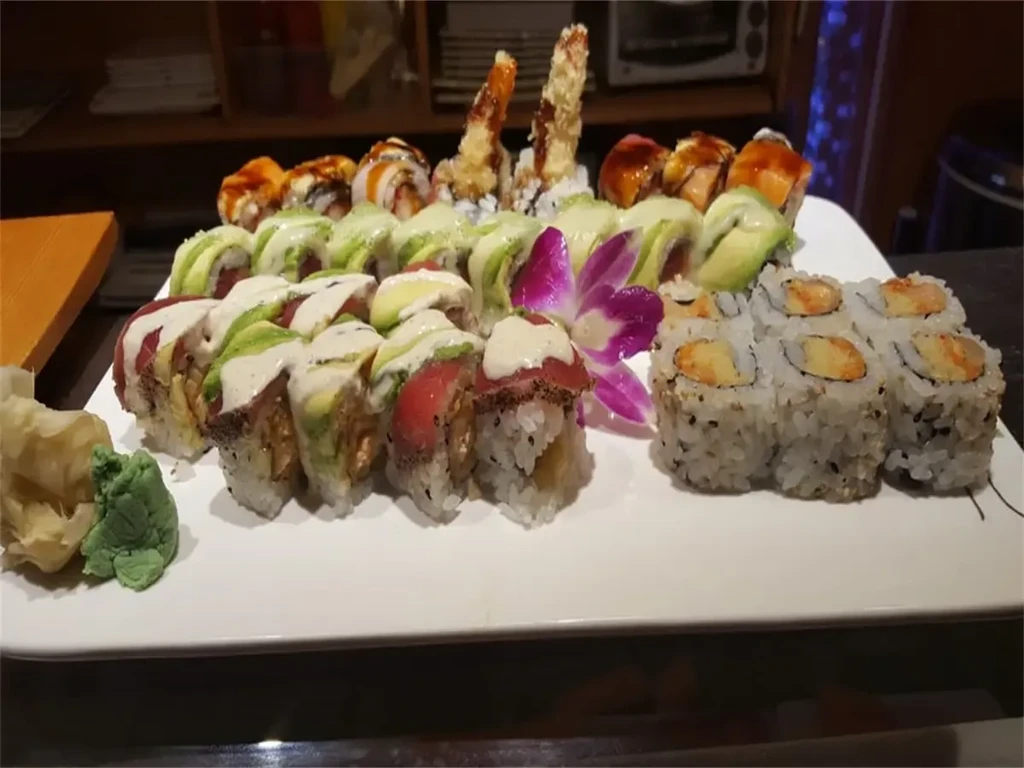 White platter with diverse sushi rolls, wasabi, ginger, purple orchid.