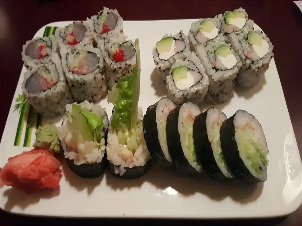 Assorted sushi rolls with wasabi and pickled ginger on a plate.