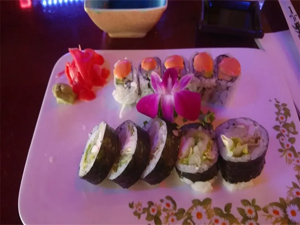A dimly lit plate of varied sushi, pink ginger, and orchid.