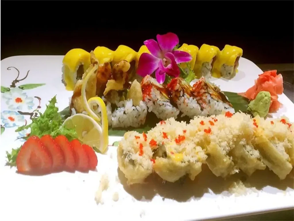 Platter of diverse sushi rolls with fruit, ginger, wasabi, and lettuce.