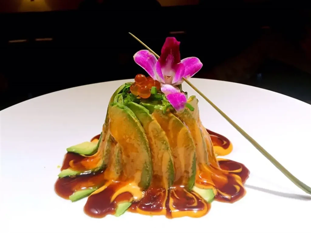 Conical avocado stack, drizzled sauces, fish roe, and orchid on plate.