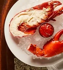 Prepared lobster tail and claw on ice with red dipping sauce.