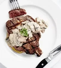 Fork pierces grilled steak with mushroom sauce, parsley, and knife.