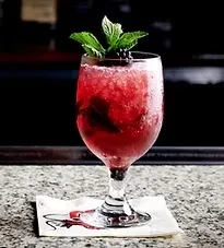 Red crushed ice drink in wine glass, garnished with mint and berries.