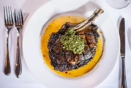 Grilled bone-in steak with green sauce on a white plate.