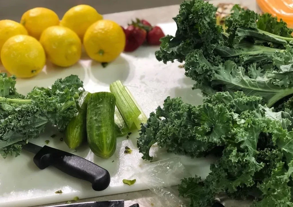Fresh kale, cucumbers, celery, lemons, strawberries, and a paring knife.