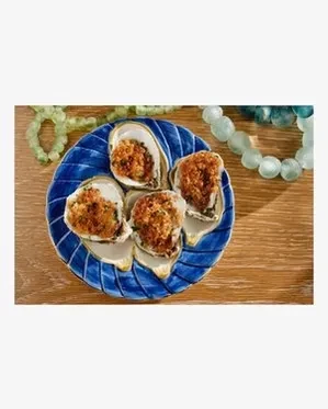 Four gratinated oysters on a ridged blue plate with green beads.