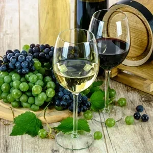 Two wine glasses, grapes, bottles, and a barrel on a wooden surface.