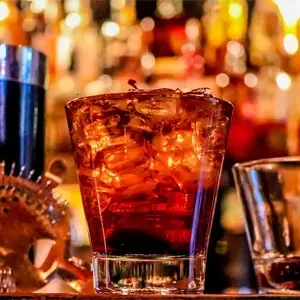 Dark red drink with ice, cherry, and cocktail shaker at a bar.