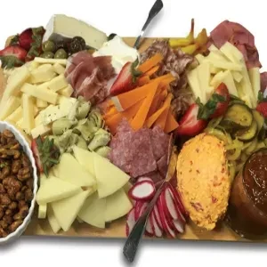Large wooden charcuterie board displaying cheeses, meats, fruits, and vegetables.