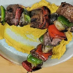 Two grilled meat and vegetable skewers with yellow puree on a plate.
