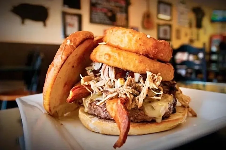 Gourmet burger with pulled pork, bacon, melted cheese, and onion rings.