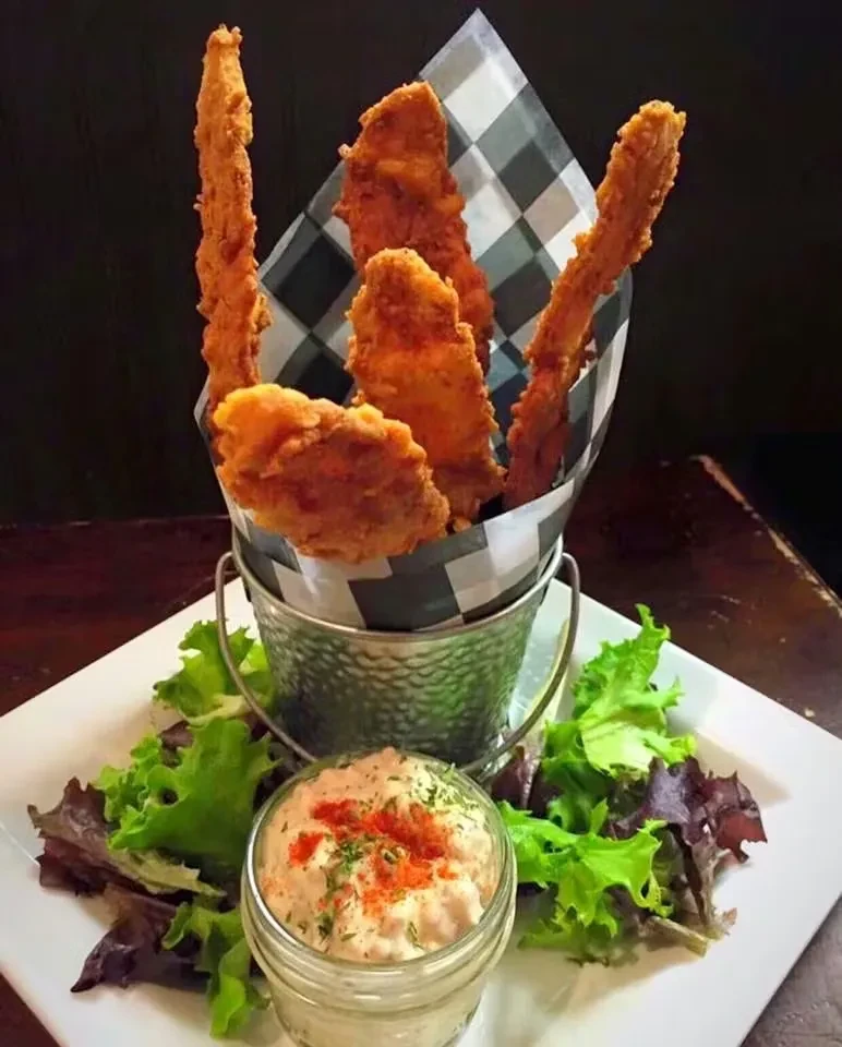 Golden-brown fried strips in a metal bucket, with sauce and salad.