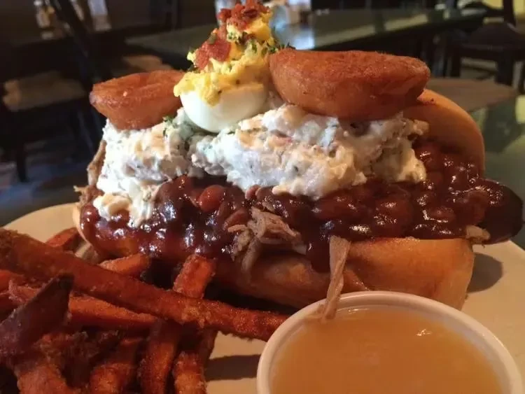 Overflowing pulled pork sandwich with deviled eggs, sweet potato fries, bacon, and chives.