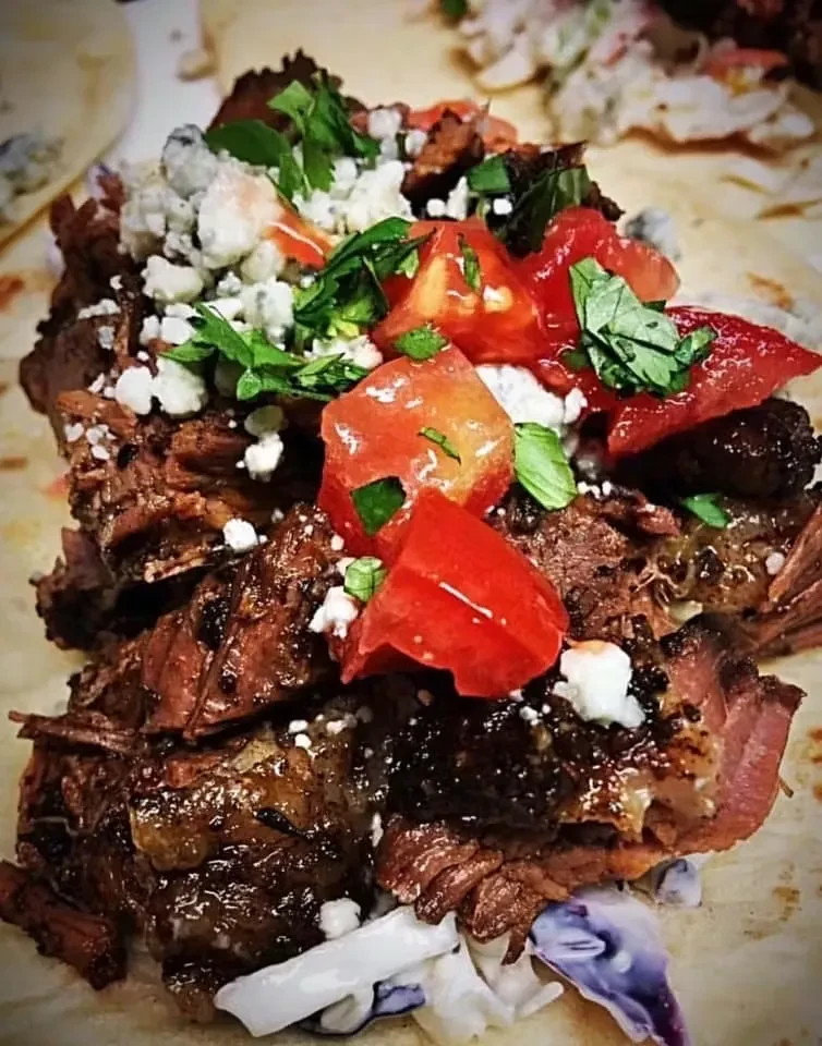 Shredded meat taco with coleslaw, diced tomatoes, white cheese, and herbs.