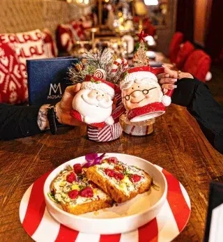 Hands 'cheers' with Santa and Mrs. Claus mugs over savory toast.