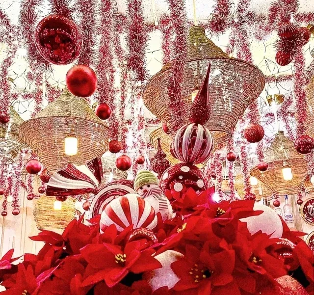 Festive interior with red tinsel, ornaments, warm lights, and poinsettias.