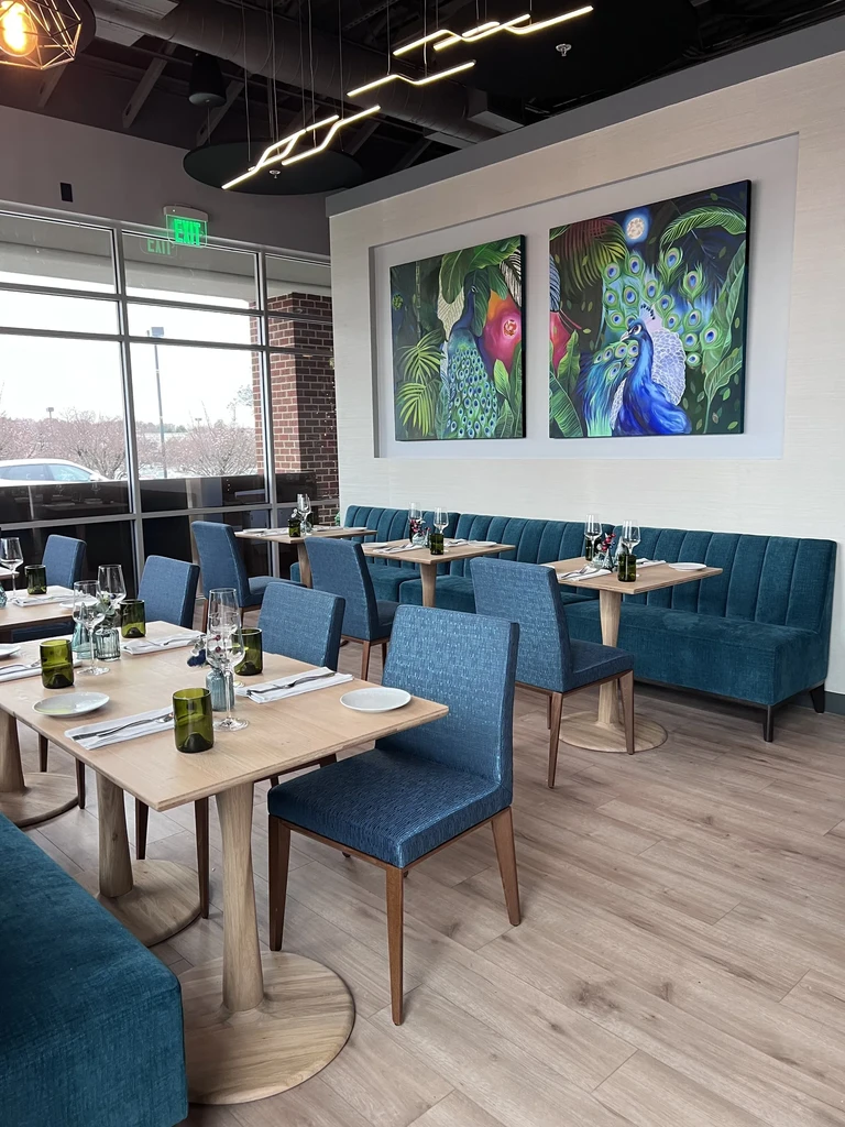 Empty modern restaurant interior with blue seating, wooden tables, and peacock art.