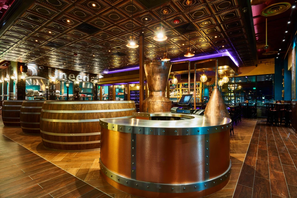 Steampunk bar with prominent copper stills, wooden barrels, and ornate ceiling.