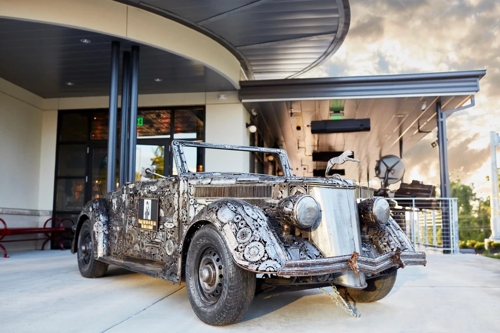 Detailed art car, welded metal mosaic, vintage style, parked at building.