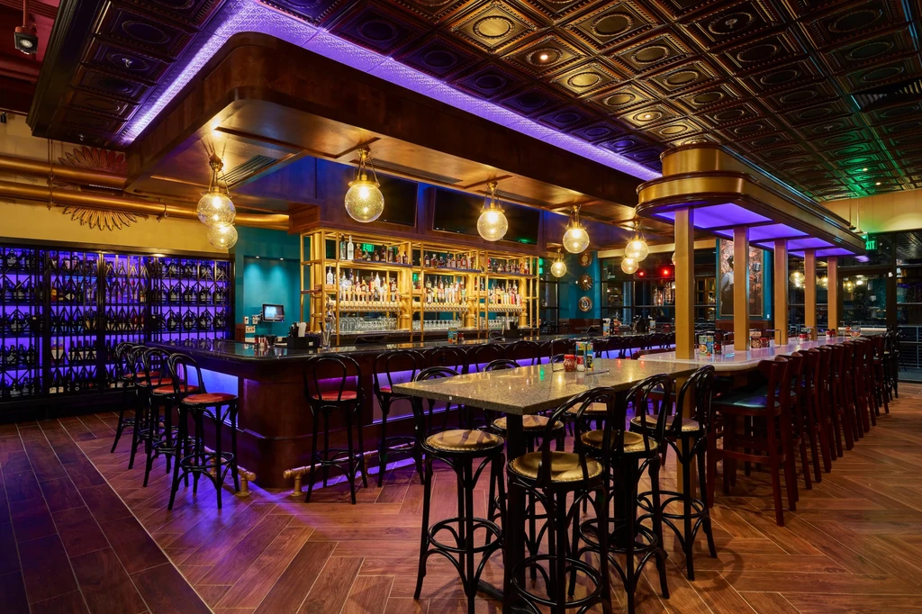 Modern bar with a long counter, liquor display, and purple-lit wine wall.