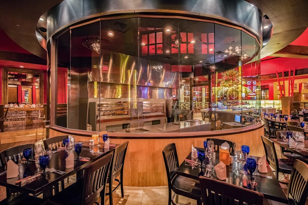 Modern restaurant dining area and kitchen separated by curved glass.