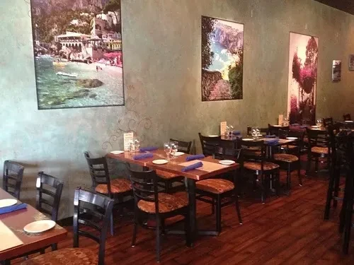 Empty restaurant dining area with set wooden tables, chairs, and artwork.