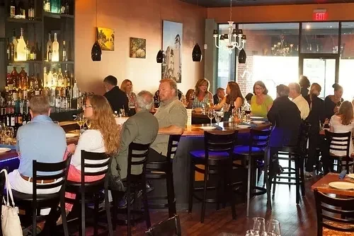 Restaurant interior features a well-lit bar, patrons, and dining tables.