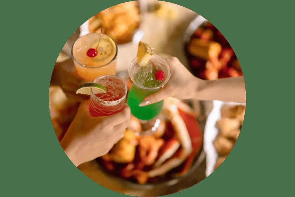Hands clinking three colorful cocktails with fruit garnishes.