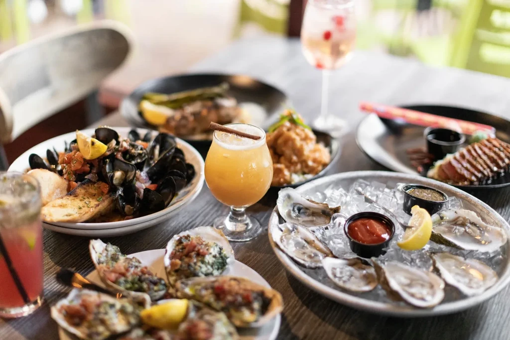 Oysters, mussels, tuna, chicken, and cocktails on a restaurant table.