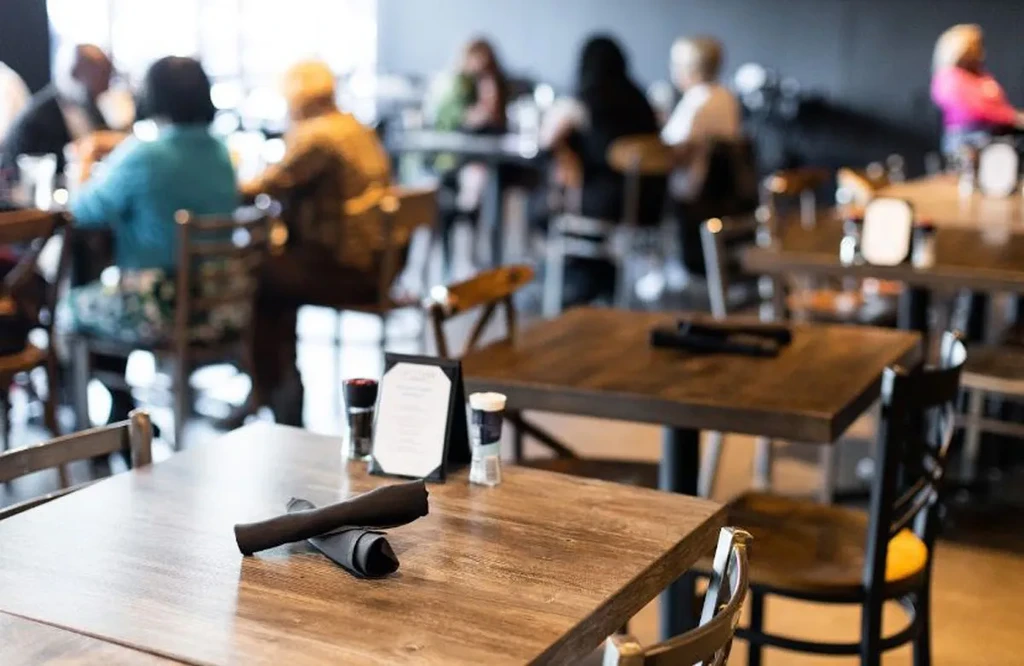 Empty wooden table with salt and pepper shakers, blurred patrons in background.