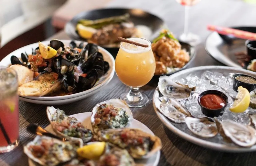 Mussels, raw and baked oysters, and cocktails on a wooden table.