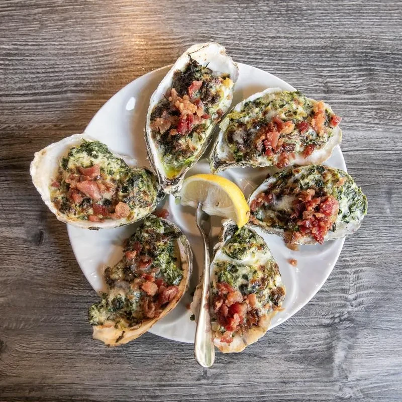 White plate with six baked oysters topped with spinach, bacon, lemon.