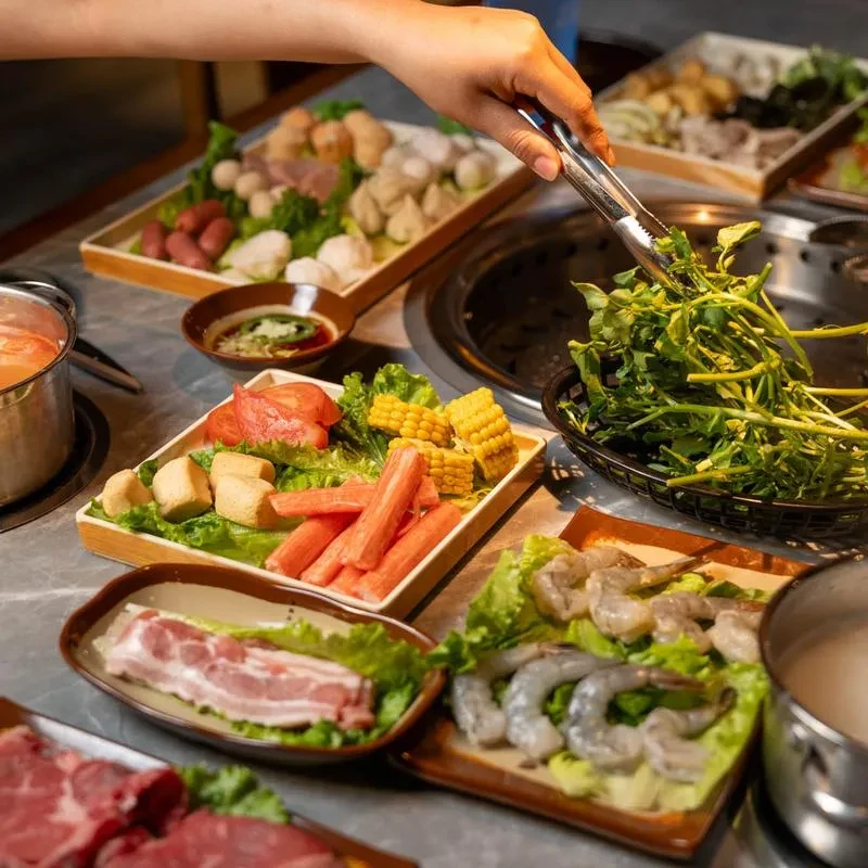 Close-up of fresh hotpot ingredients with a hand adding vegetables.