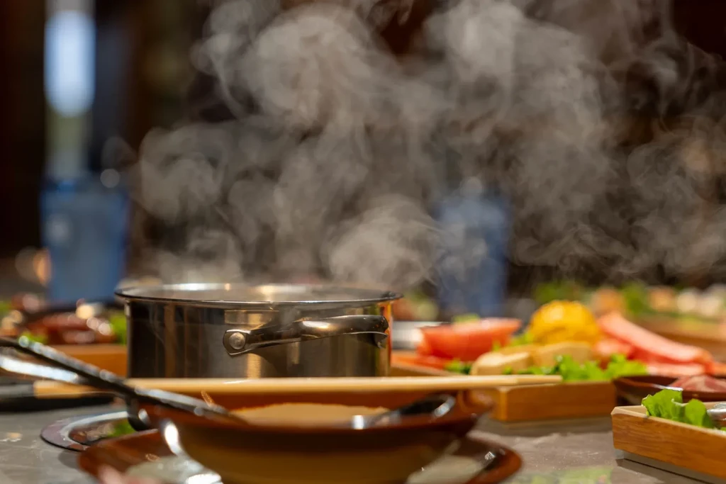 Hotpot steaming vigorously, surrounded by ingredients, a bowl, and chopsticks.