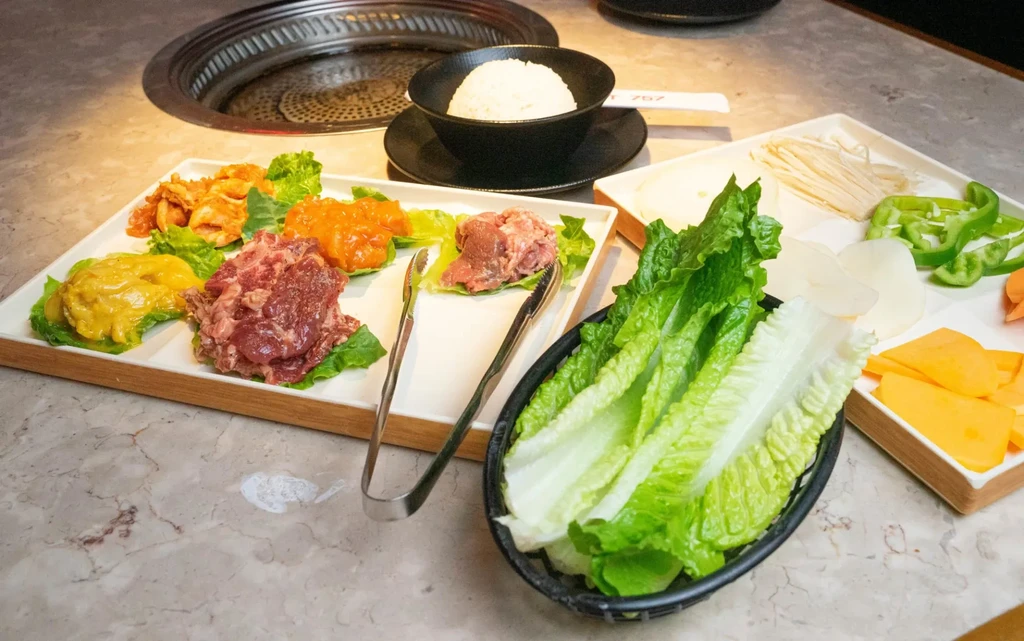 Korean BBQ spread with raw meats, fresh vegetables, rice, and grill.