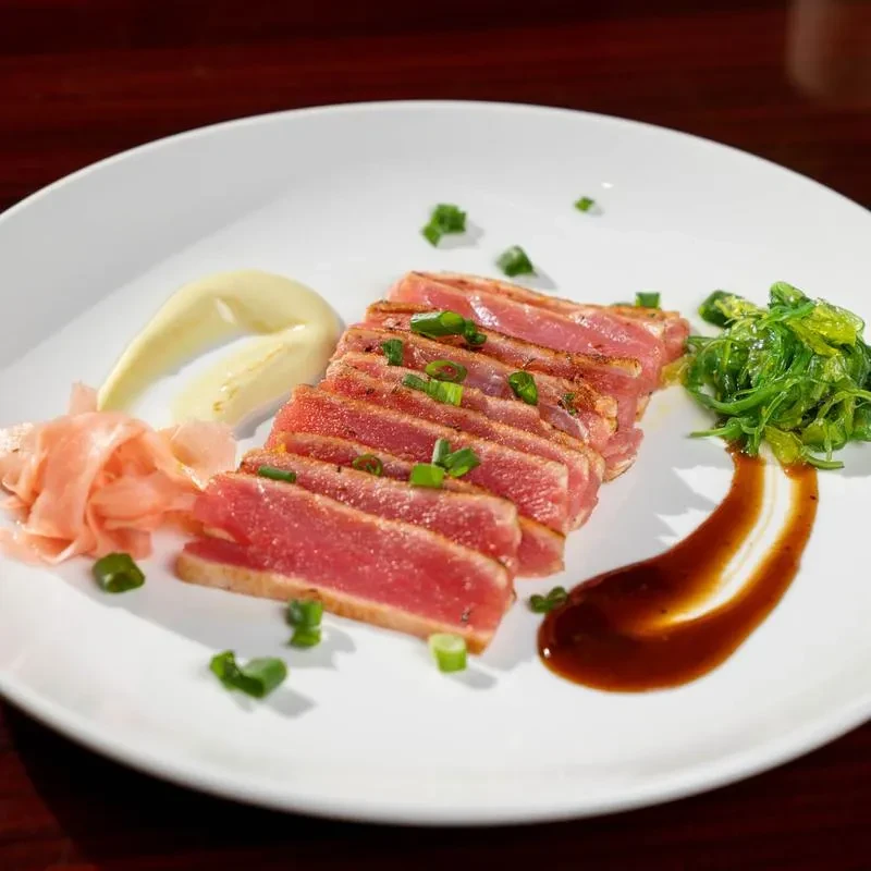Sliced rare seared tuna with sauces, pickled ginger, and seaweed salad.