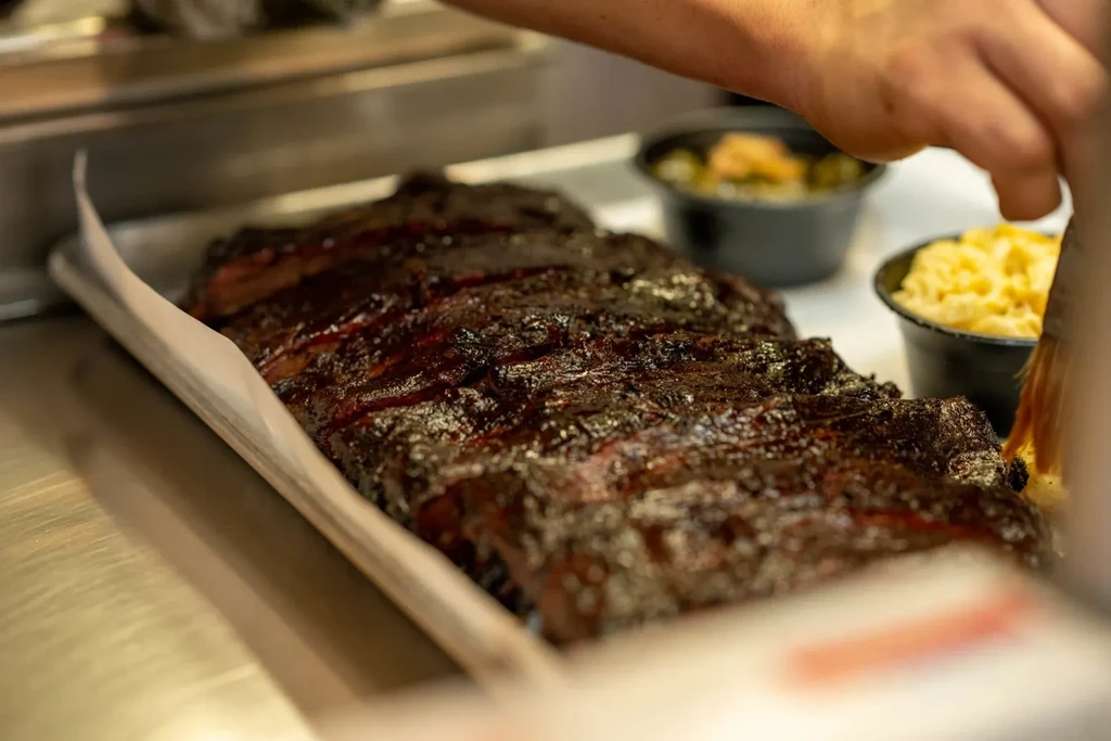 Glistening barbecued ribs on a tray, with mac and cheese and vegetables.