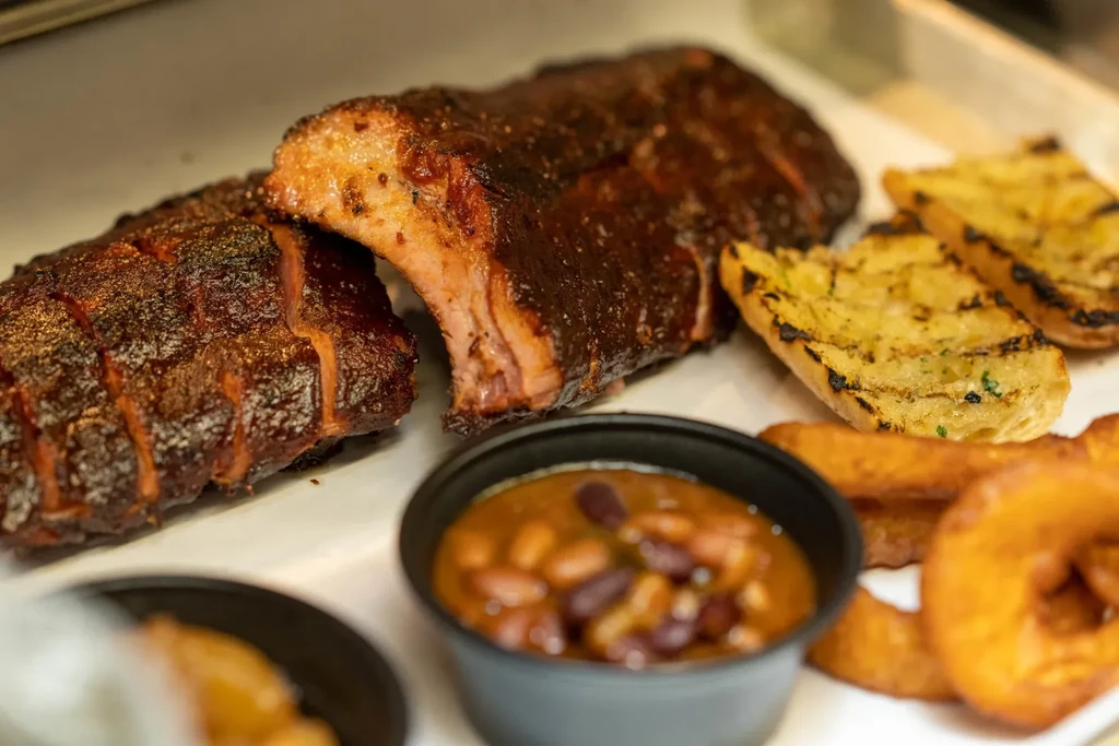 Close-up of barbecued ribs, grilled garlic bread, baked beans, and onion rings.